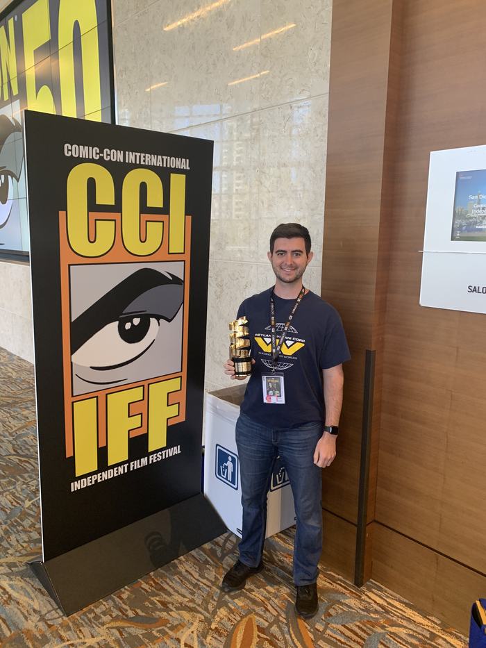 Reid Nicewonder holding the Best Documentary award next to a Comic-Con International Independent Film Festival banner