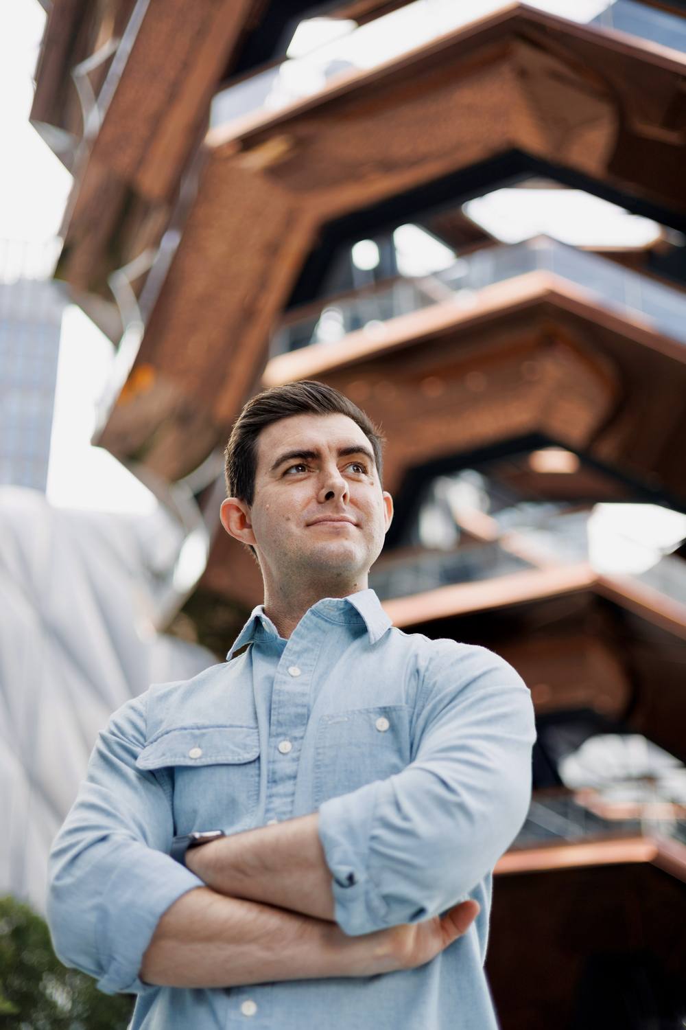Reid Nicewonder in a blue chambray shirt, arms crossed, in front of The Vessel in New York City